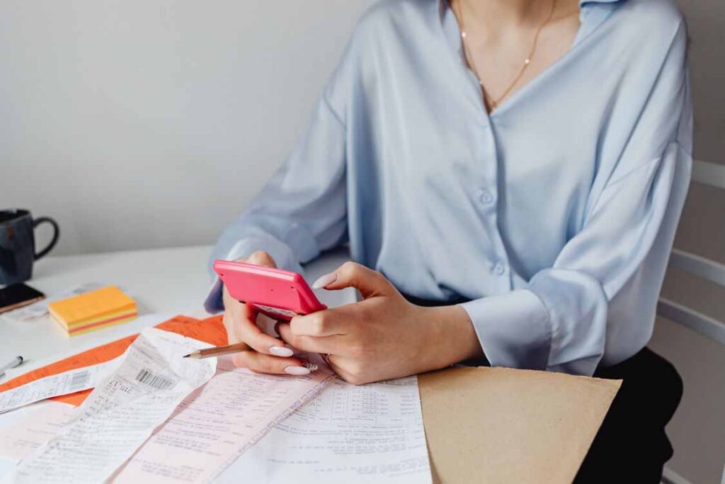 Business owner reviewing receipts and financial records while using a phone, representing cash flow planning and business coaching for SMEs.